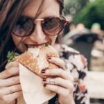 young woman eating burger عادات غذائية عليك تجنبها من أجل نظام مناعي أفضل! مجلة نقطة العلمية