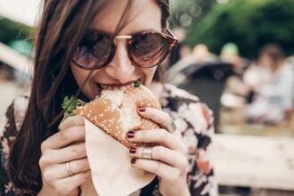 young woman eating burger عادات غذائية عليك تجنبها من أجل نظام مناعي أفضل! مجلة نقطة العلمية