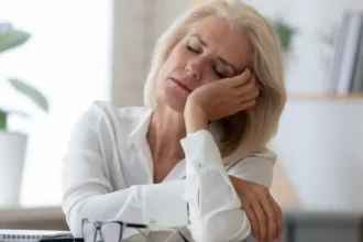 mature woman falling asleep at desk menopause insomnia concept ما هو "أرق انقطاع الطمث" وكيف تخففين أعراضه؟ مجلة نقطة العلمية