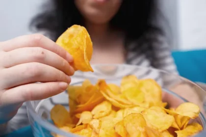 woman eating potato chips bowl الأطعمة فائقة المعالجة تزيد من خطر موتك حتى لو كنت نباتيًا! مجلة نقطة العلمية
